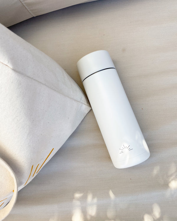 Reusable ceramic water bottle in cloud white colour by The July Co in collaboration with Frank Green. Stainless steel bottle with a ceramic lining, triple walled, spill and leak proof, keeps beverages hot or cold and features an engraved sun logo design.